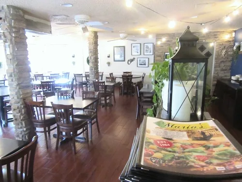 The dining room, with stone pillars, wood tables and chairs and string lights, and a stack of menus in the foreground