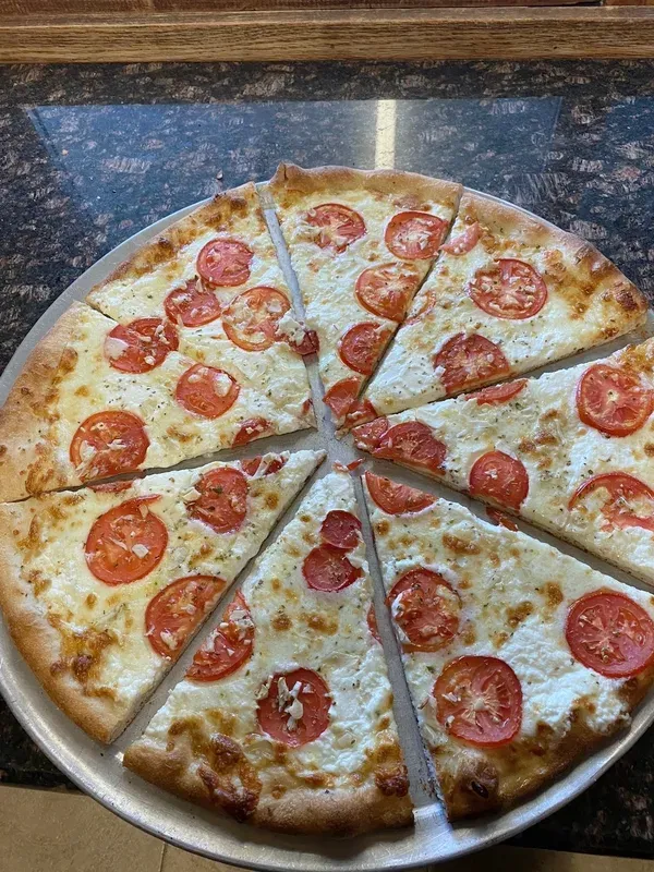 A round cheese pizza topped with sliced tomatoes, cut into eight slices on a pan