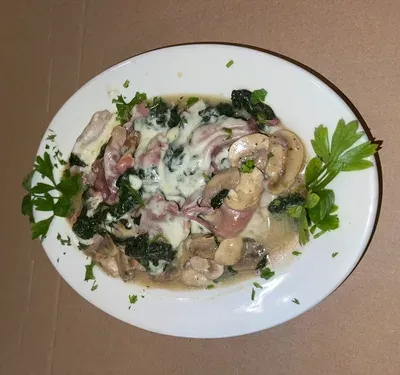 A plated entrée with ham, wilted spinach, mushrooms and melted cheese