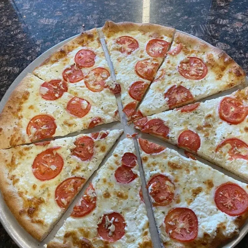 A round cheese pizza topped with sliced tomatoes, cut into eight slices on a pan