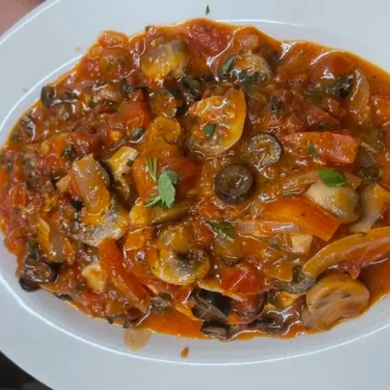 Mushrooms, black olives and peppers in tomato sauce on an oval plate