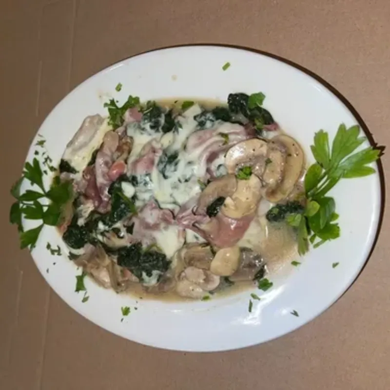 A plated entrée with ham, wilted spinach, mushrooms and melted cheese
