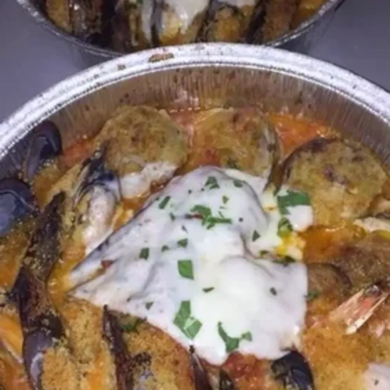 Baked mussels and stuffed clams in red sauce under melted cheese, in two foil trays