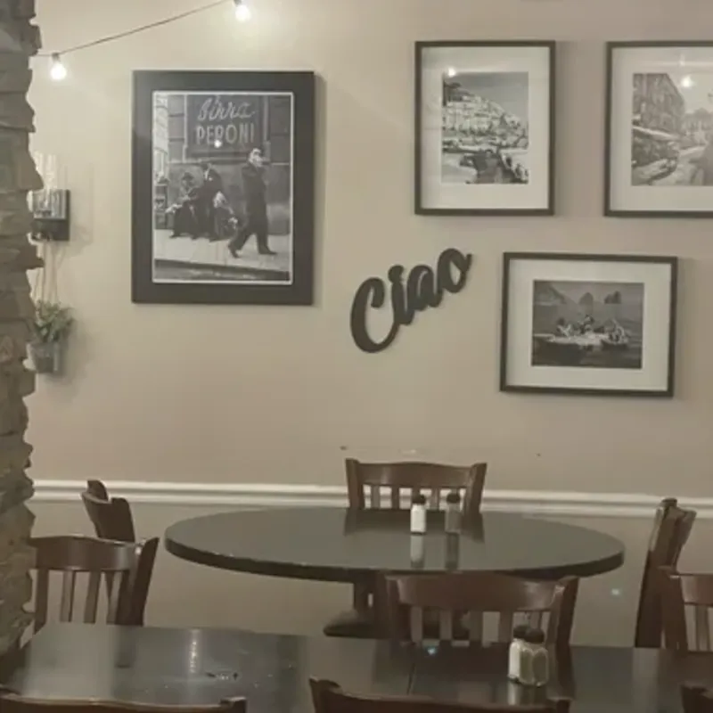 A dining-room wall of framed black-and-white photographs and a Ciao sign above tables and chairs